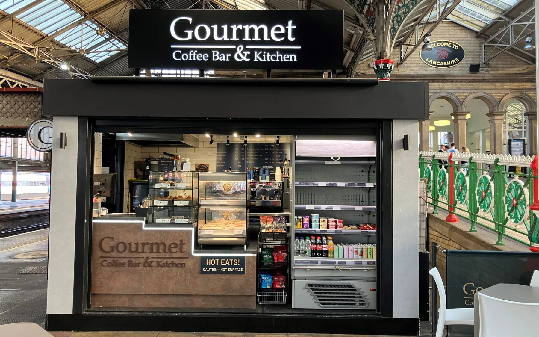 A black Gourmet kiosk with food and drink on display inside a station